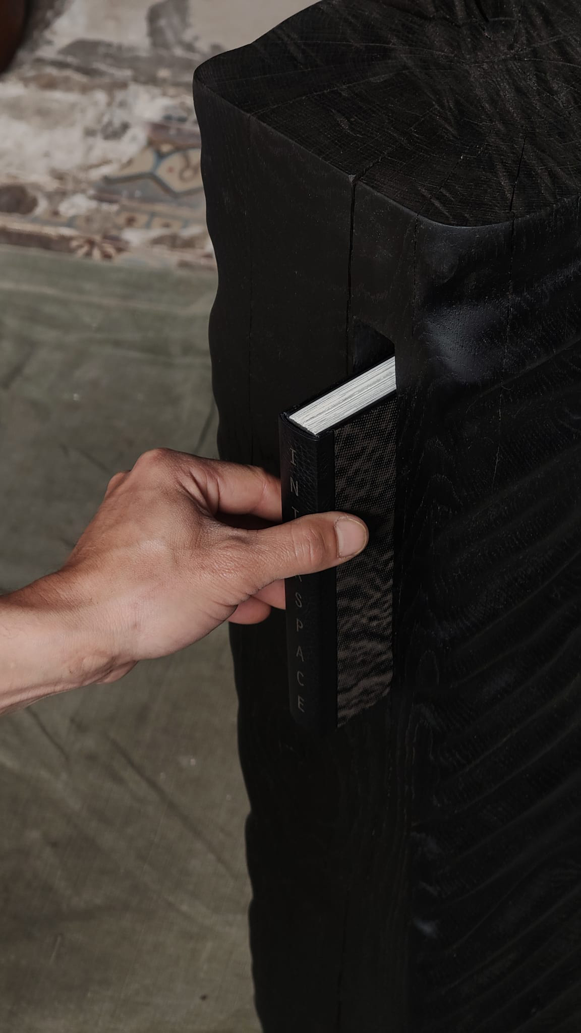 Detail of Monolith Library II by Camille Tan showing ebonised oak surface and a hand placing a book inside 